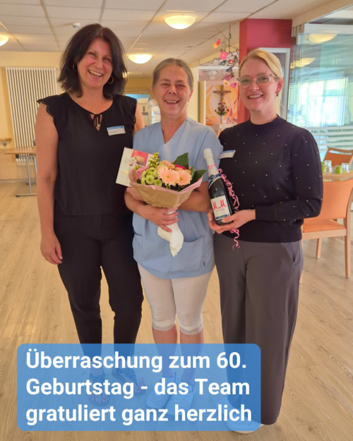 Zwei Frauen gratulieren einer Kollegin zum Geburtstag inklusive Blumenstrauß, Sekt und etwas Süßes. Bildbeschriftung: Überraschung zum 60. Geburtstag - das Team gratuliert ganz herzlich