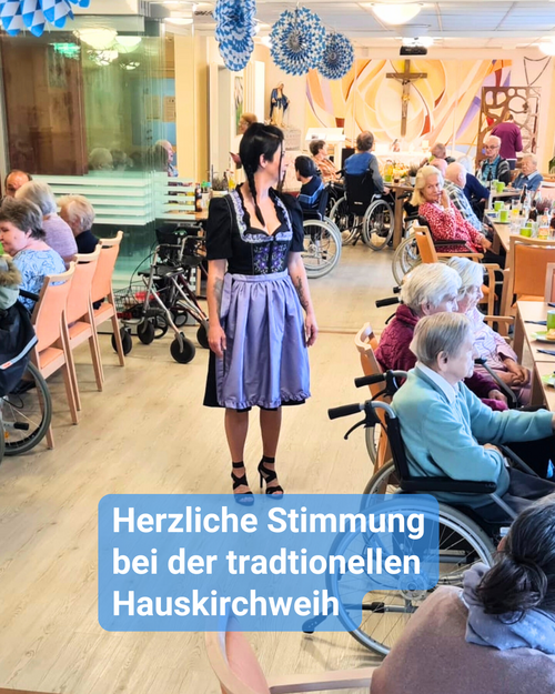 Eine Gruppe Senioren und Seniorinnen feiert ein Fest und genießt gemeinsam Getränke und Speisen. Inmitten von ihnen ist eine Betreuungskraft im traditionellen Dirndl. Bildbeschriftung: Herzliche Stimmung bei der traditionellen Hauskirchweih